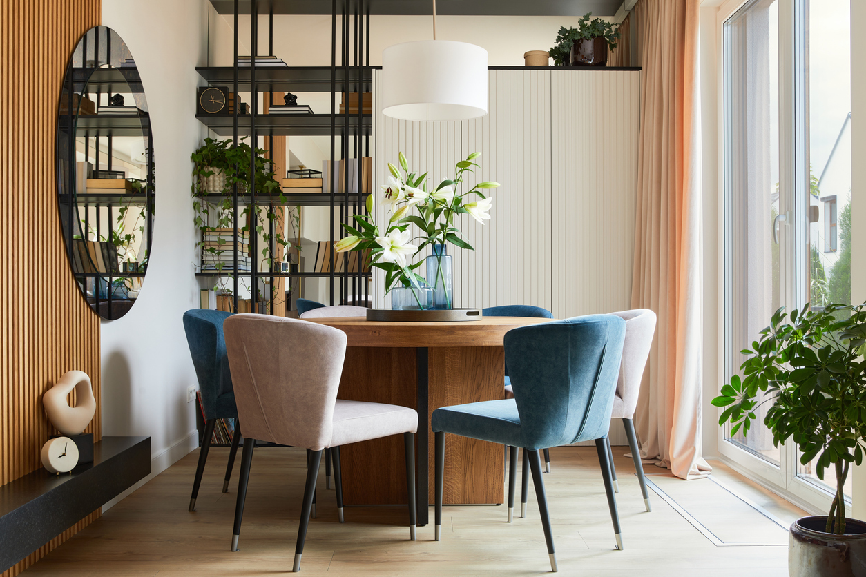Stylish composition of elegant dining room interior design with velvet armchairs, design rounded wooden table and beautiful personal accessories. Glamour interior design inspiration. Template.